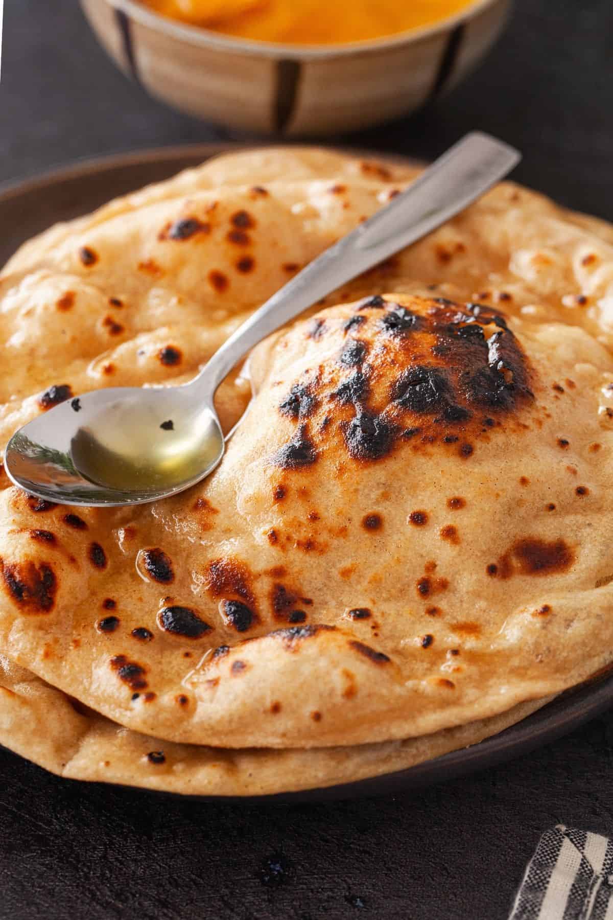 A stack of tandoori roti with a ghee spoon.