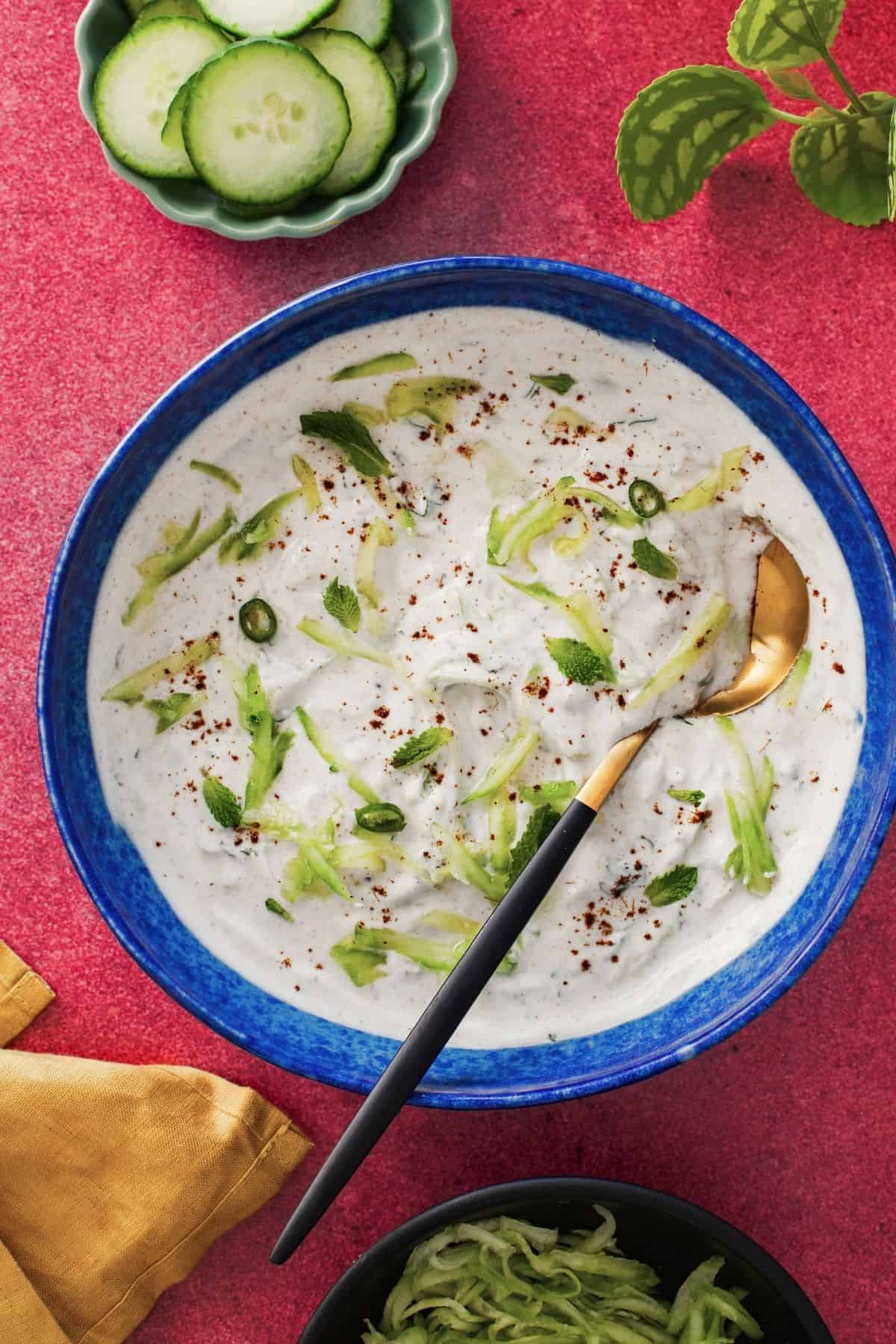 Cucumber yogurt in a blue bowl on a pink background.