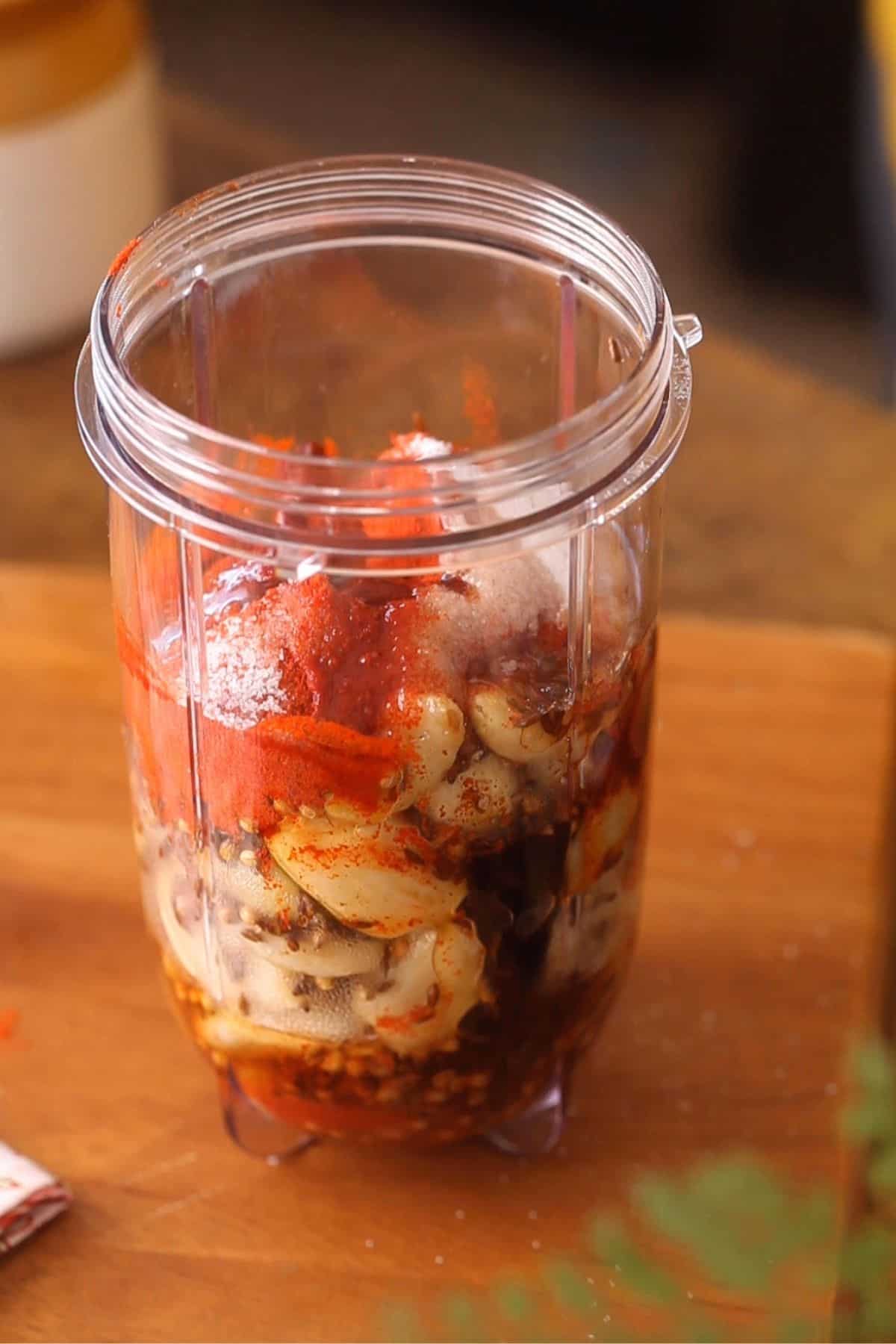 Adding garlic, chili powder, vinegar and salt to a blender jar.