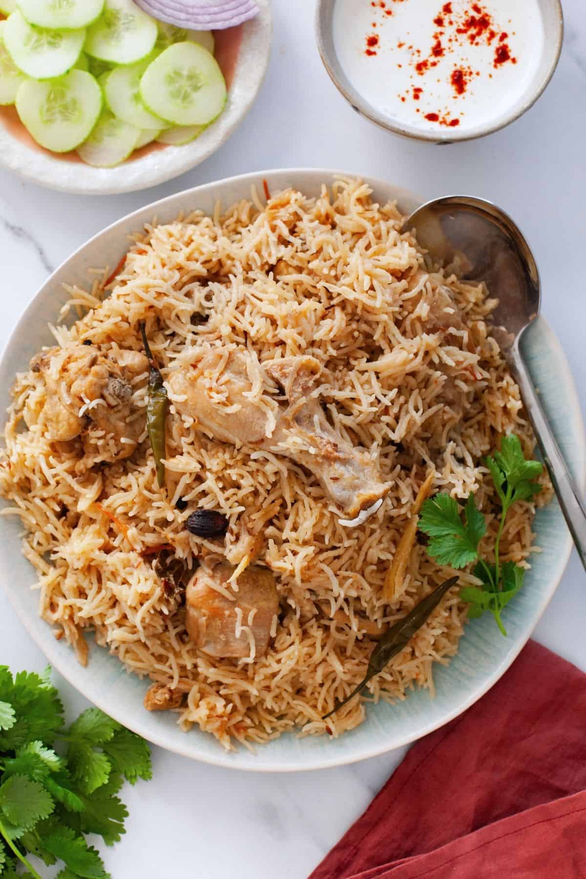 Chicken pulao plated in a blue platter and served with salad and yogurt.