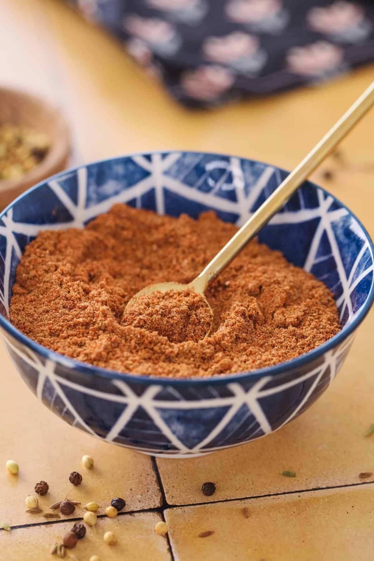 Chaat Masala Powder in a blue bowl with gold teaspoon.