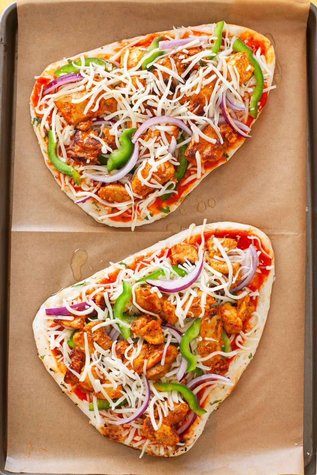 Two naan chicken pizza placed on a baking tray and ready to bake. 