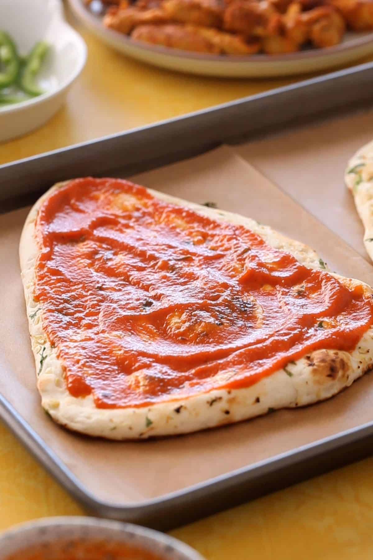 Garlic naan spread with tomato sauce.