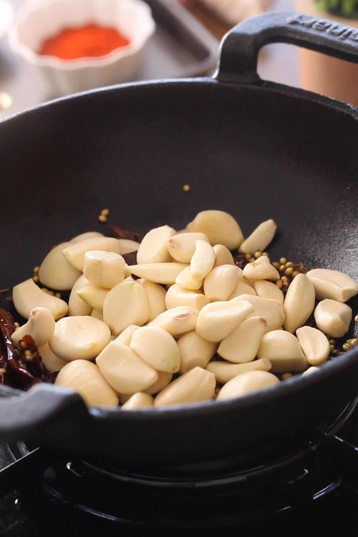 Adding raw garlic pods to spices and red chilies.
