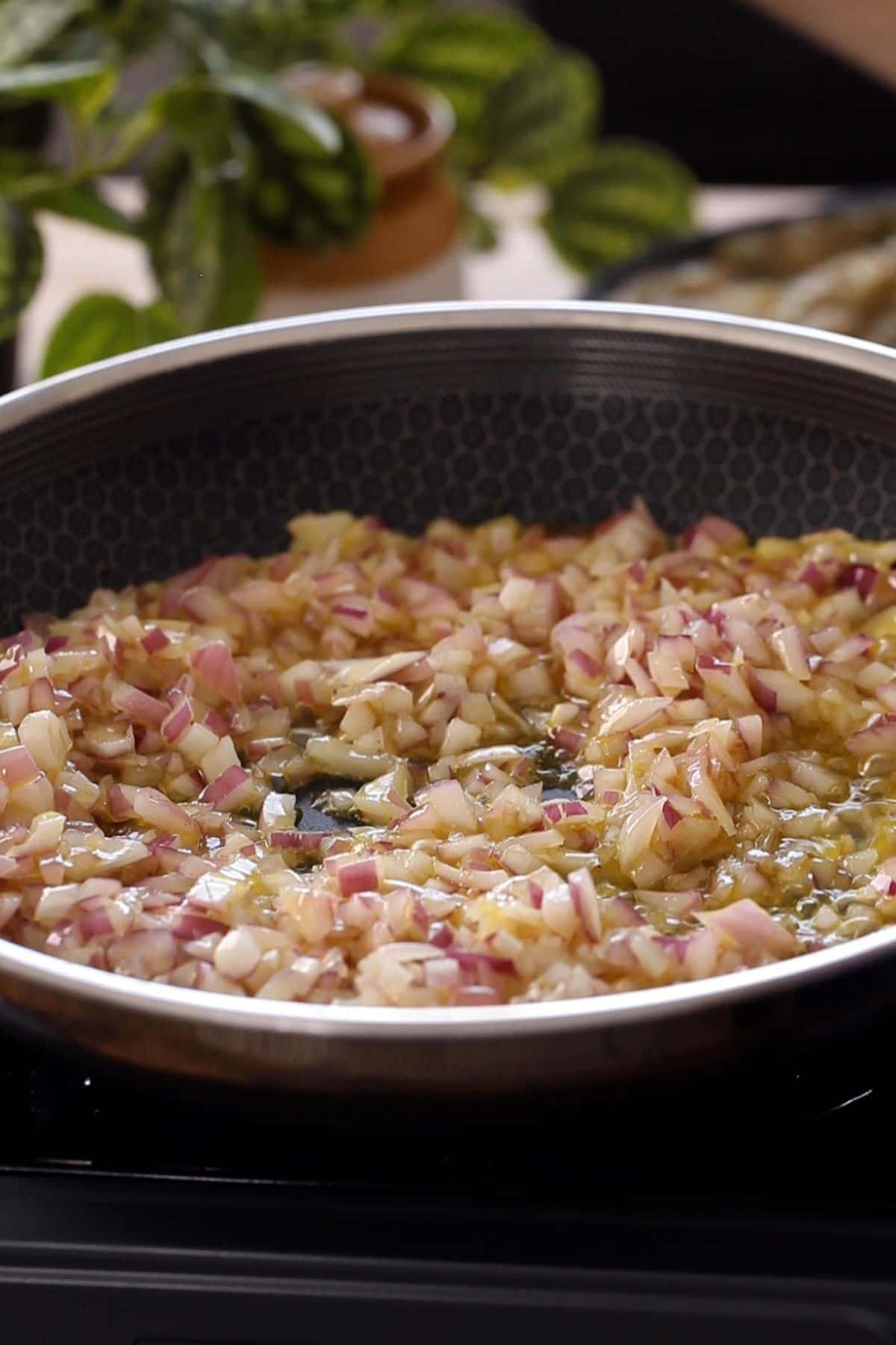 Chopped onions frying in oil in a black pan.