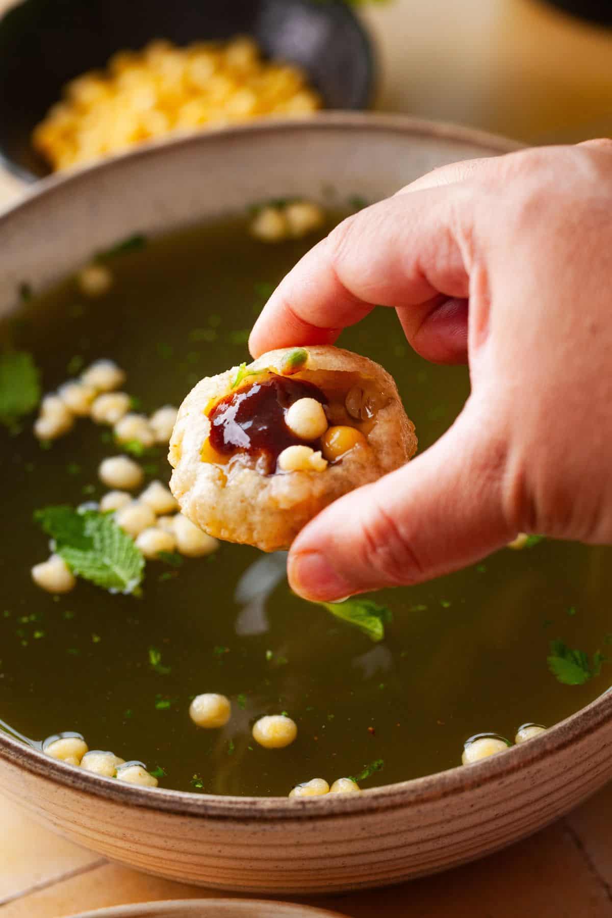 Holding a pani puri filled with tamarind chutney, stuffing and tangy water. 