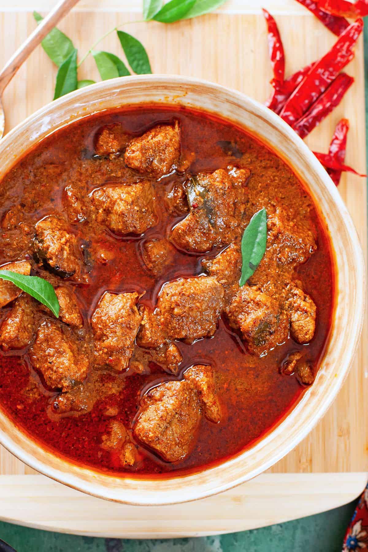 Close up of lamb vindaloo plated in a beige ceramic bowl.