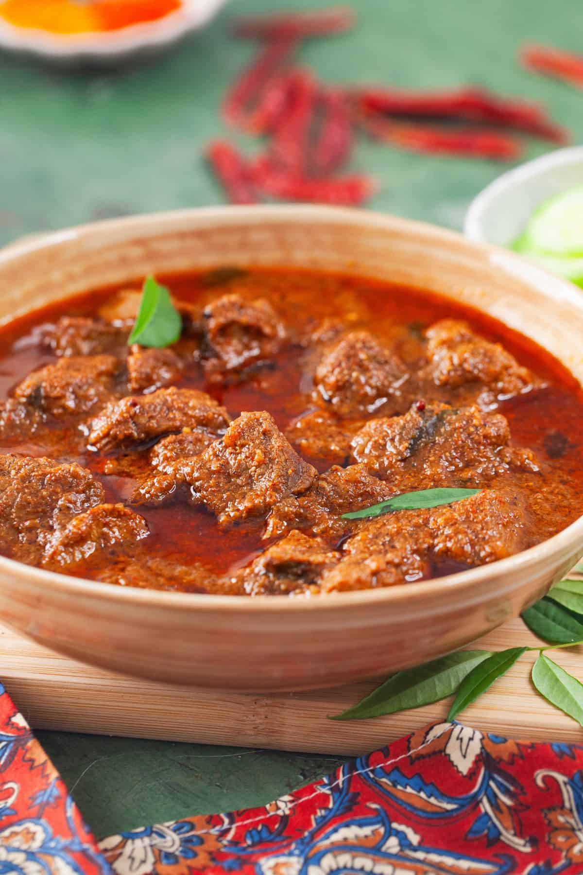 Side image of vindaloo lamb curry with red chili peppers in background.