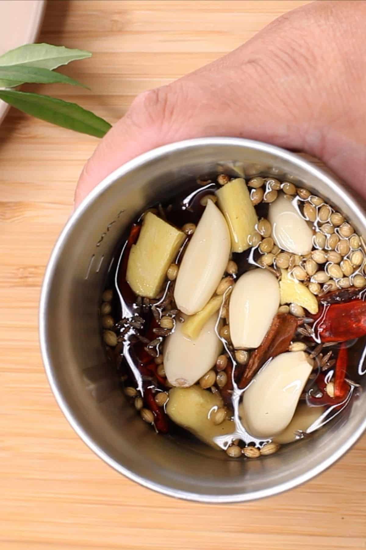 Whole spices, ginger and garlic are added to the soaked red chilies.