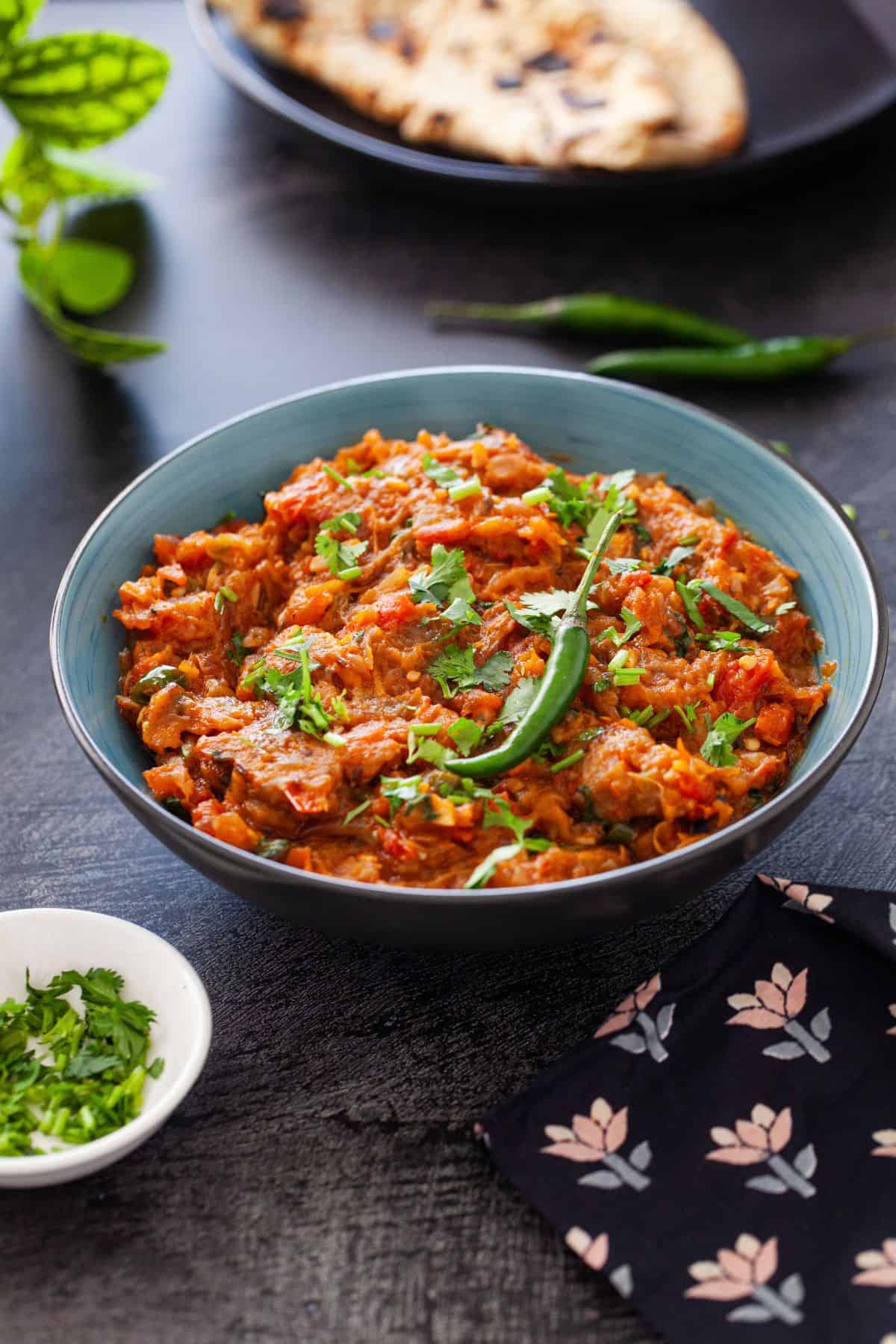Baingan Bharta served in a blue and black bowl and placed on a black background.