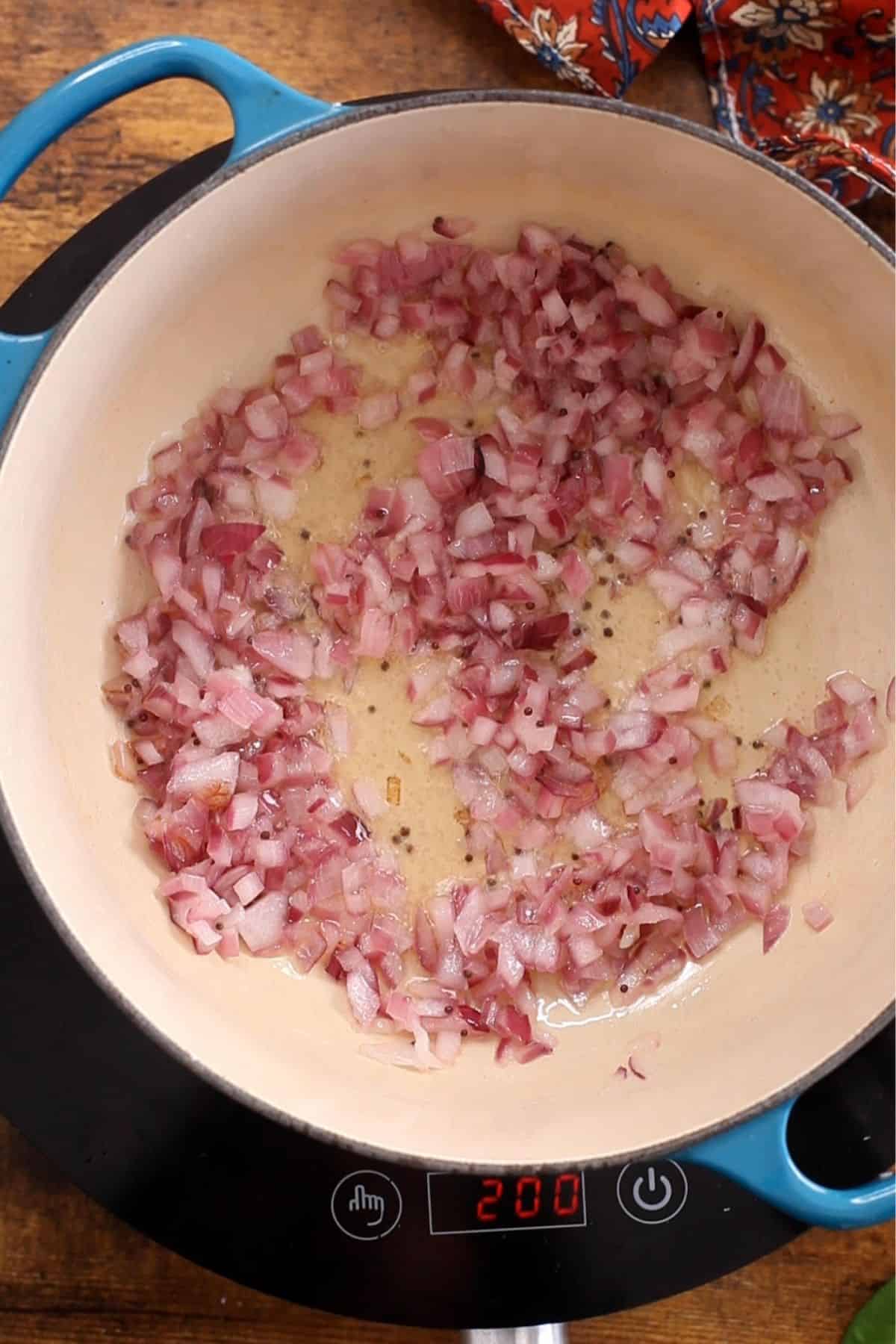 Browned onions and black mustard seeds in a dutch oven pot.
