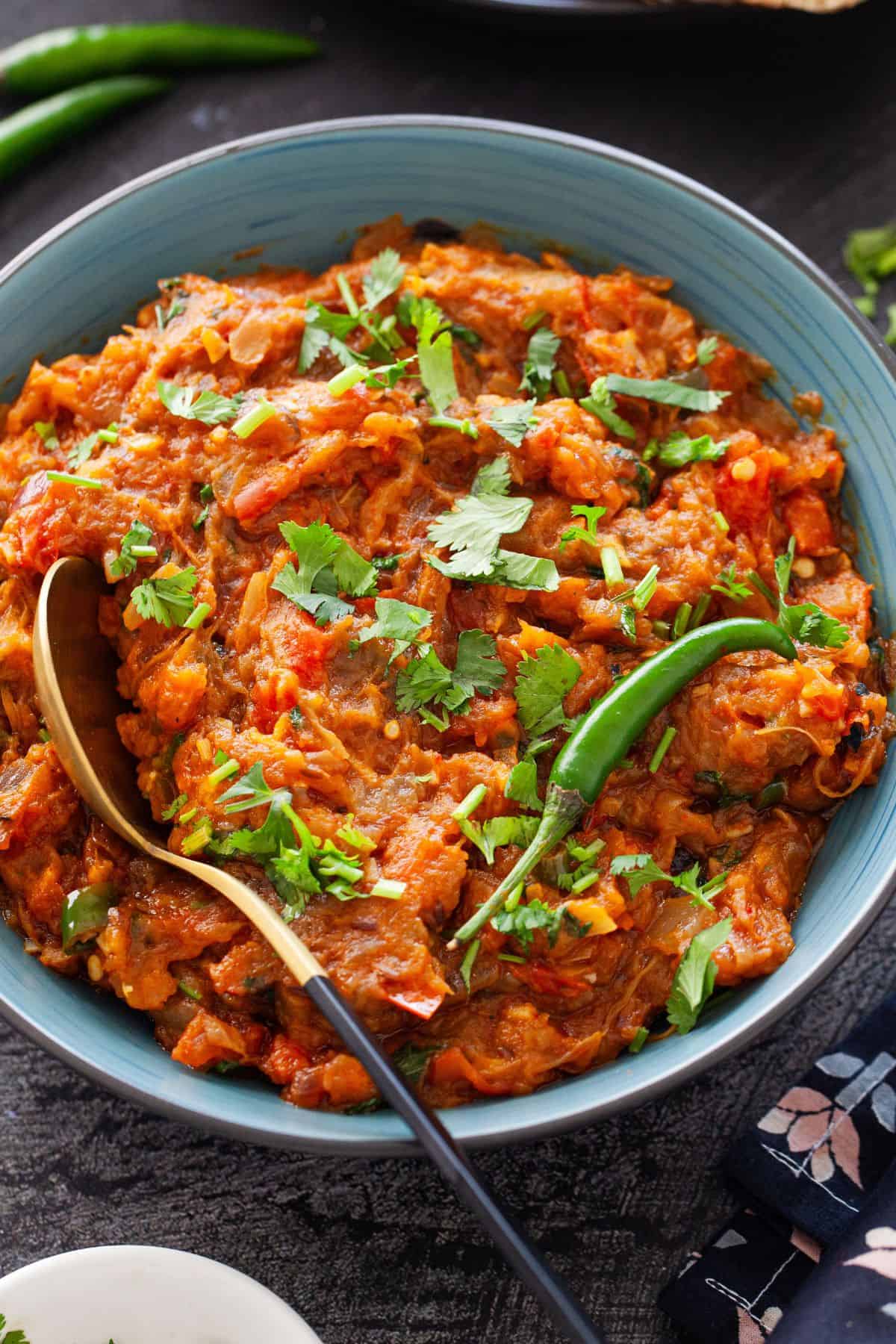 Roasted mashed eggplant curry served in a black and blue bowl with a golden spoon.