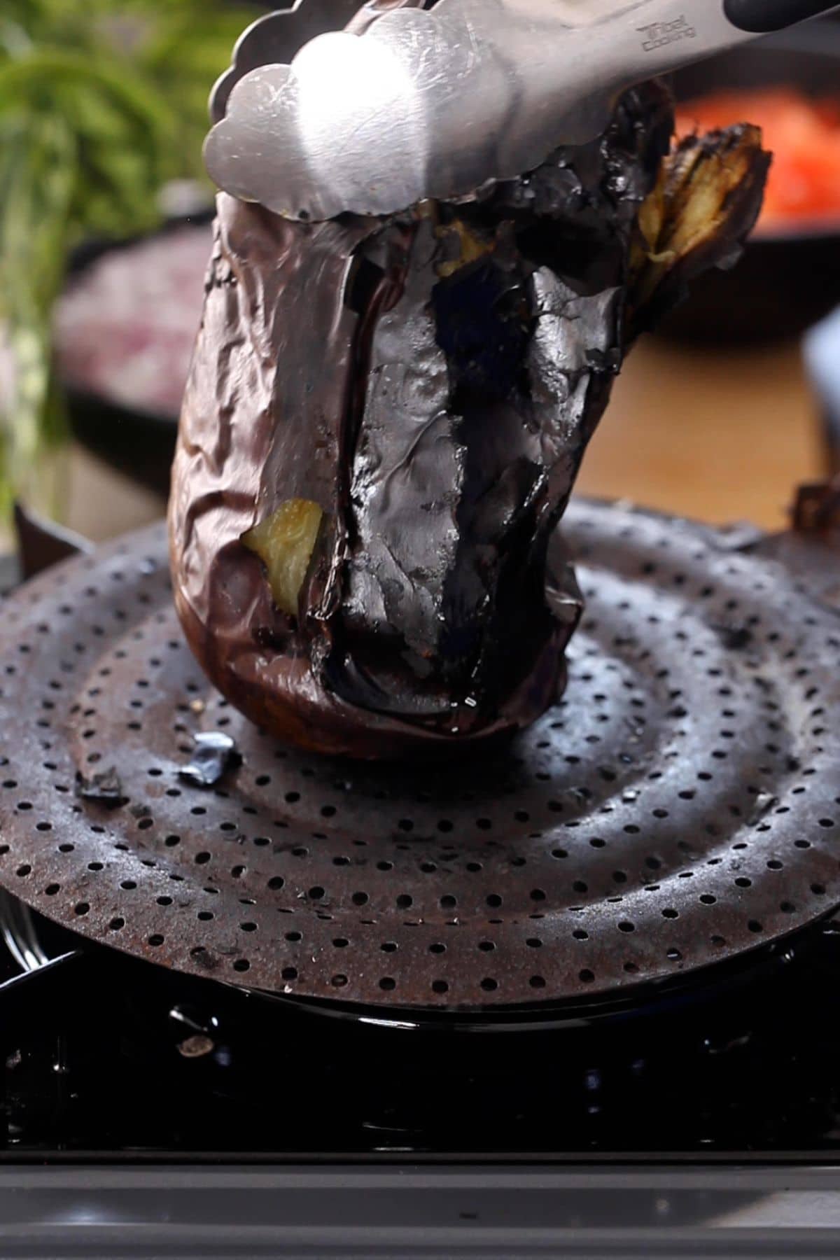 Holding eggplant with tongs to roast it on all sides.