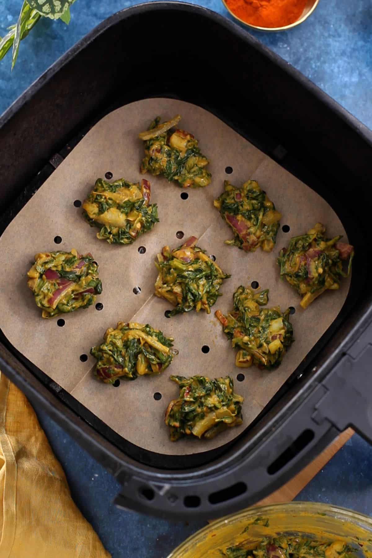 Palak pakoras are placed on an air fryer basket.