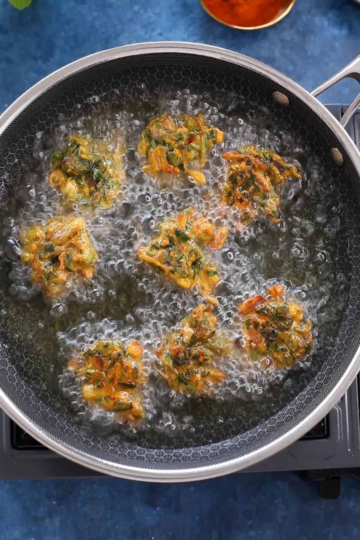 Golden brown spinach pakoras sizzling in hot oil.