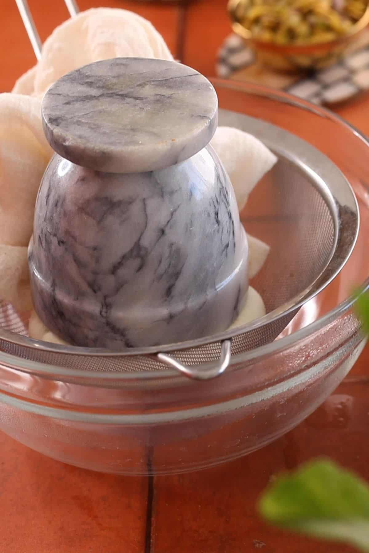 Weighing down the chenna so that excess moisture is removed.