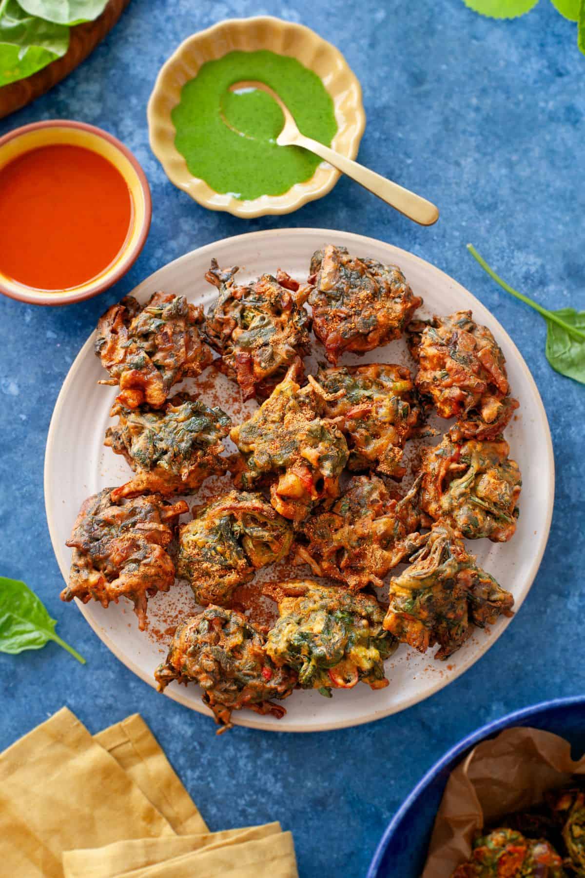 Spinach Pakora served on a beige plate with green chutney and ketchup.