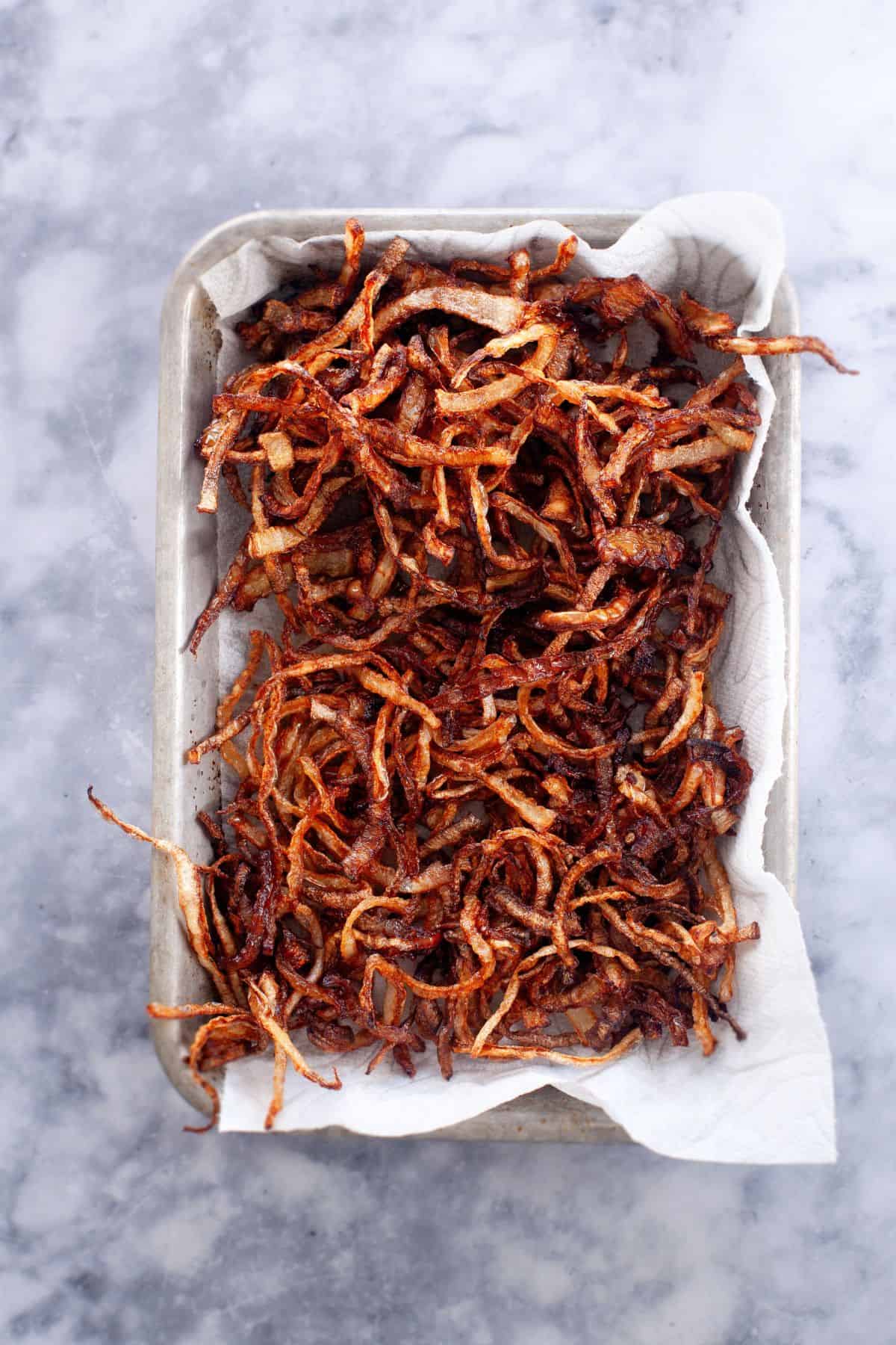 Deep fried onions placed on a paper towel lined baking tray.