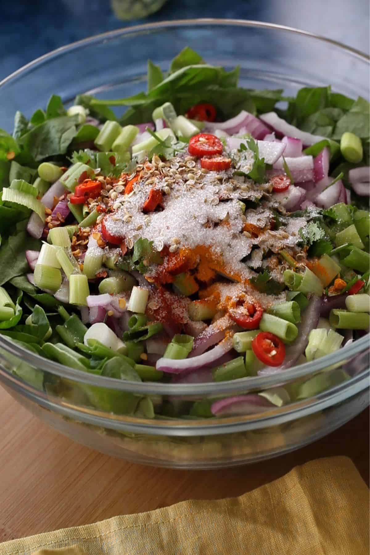Spinach and onions with spicesm cilantro and chilies in a large glass bowl.