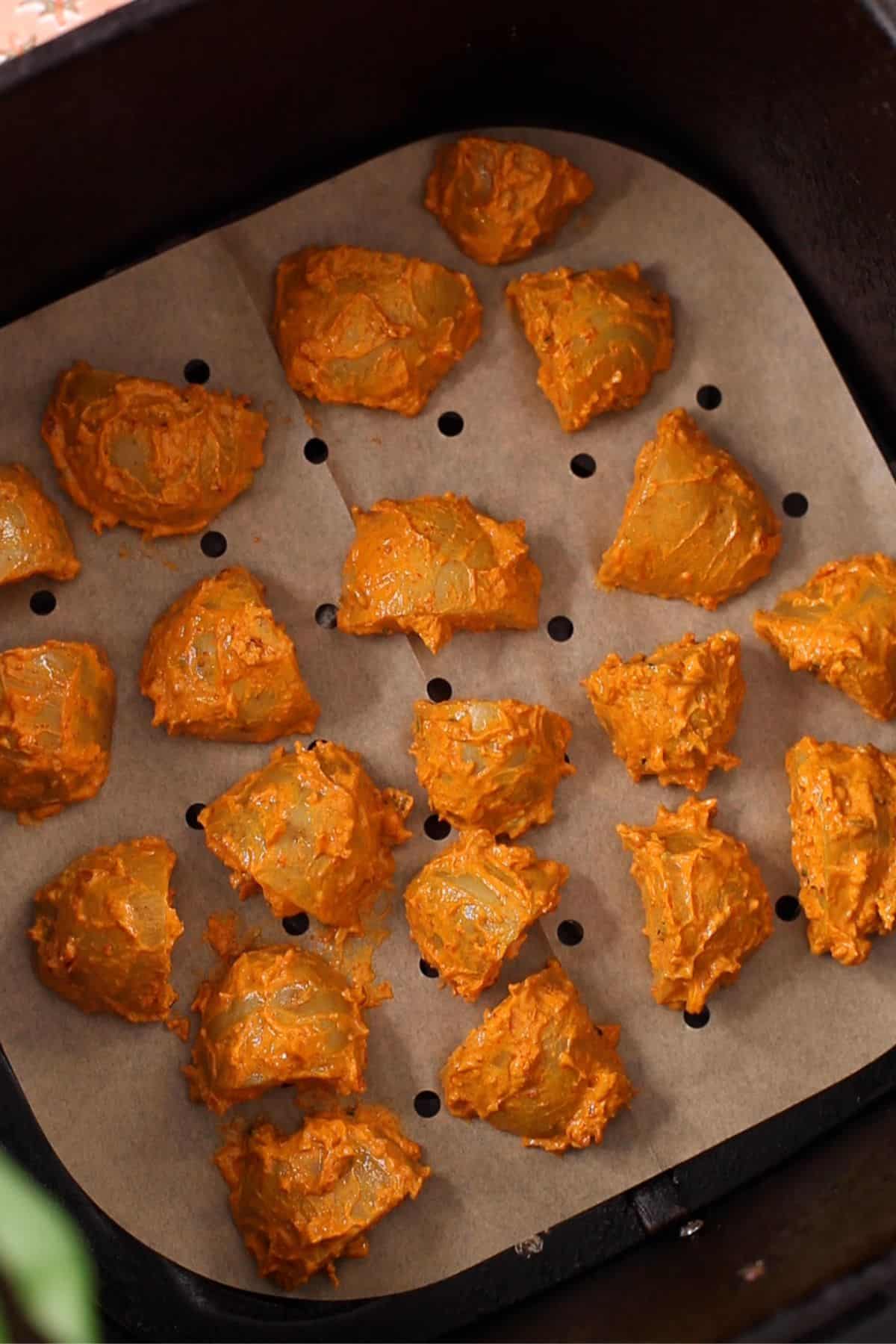 Marinated achari potatoes are placed in the air fryer basket in a single layer.