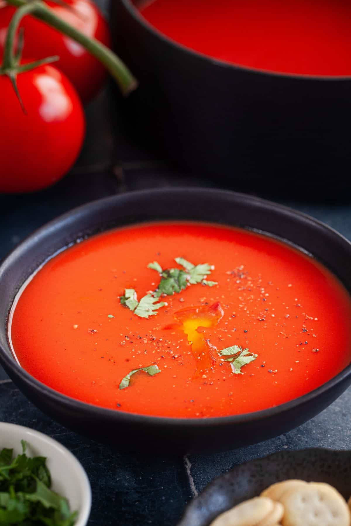 Indian tomato soup in a black bowl with fresh tomatoes in background.