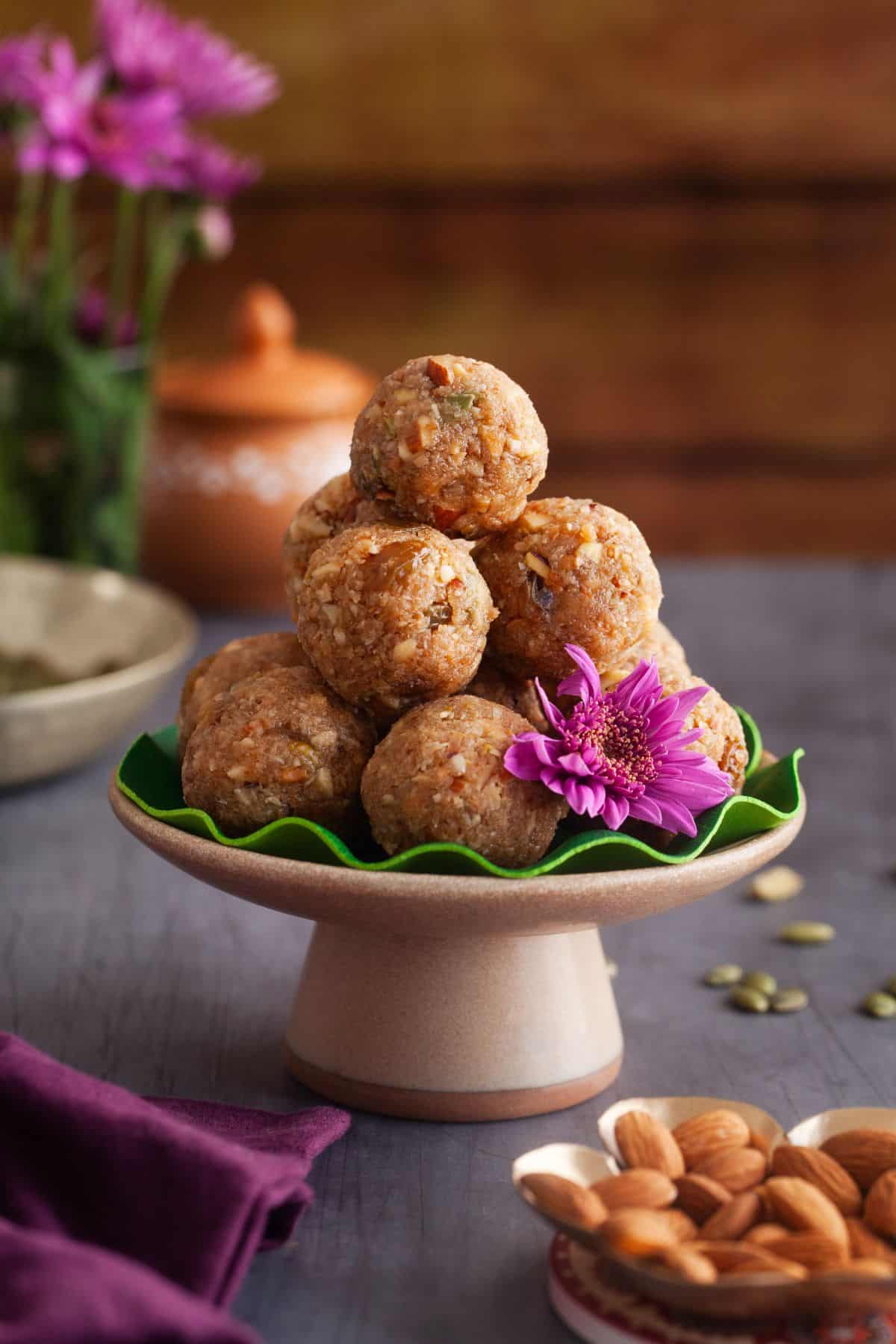 Stack of jaggery coconut ladoo on a brown stand with purple flowers in background.