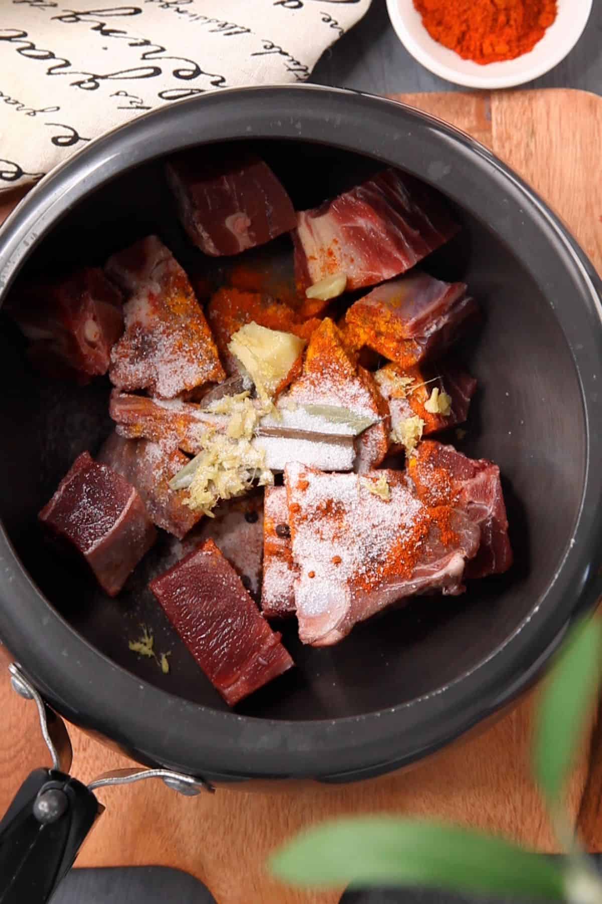 Goat meat in a black pressure cooker with ginger, garlic, salt and spices.
