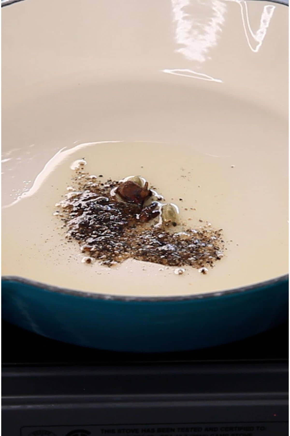 Whole spices and black pepper powder in cooking oil.