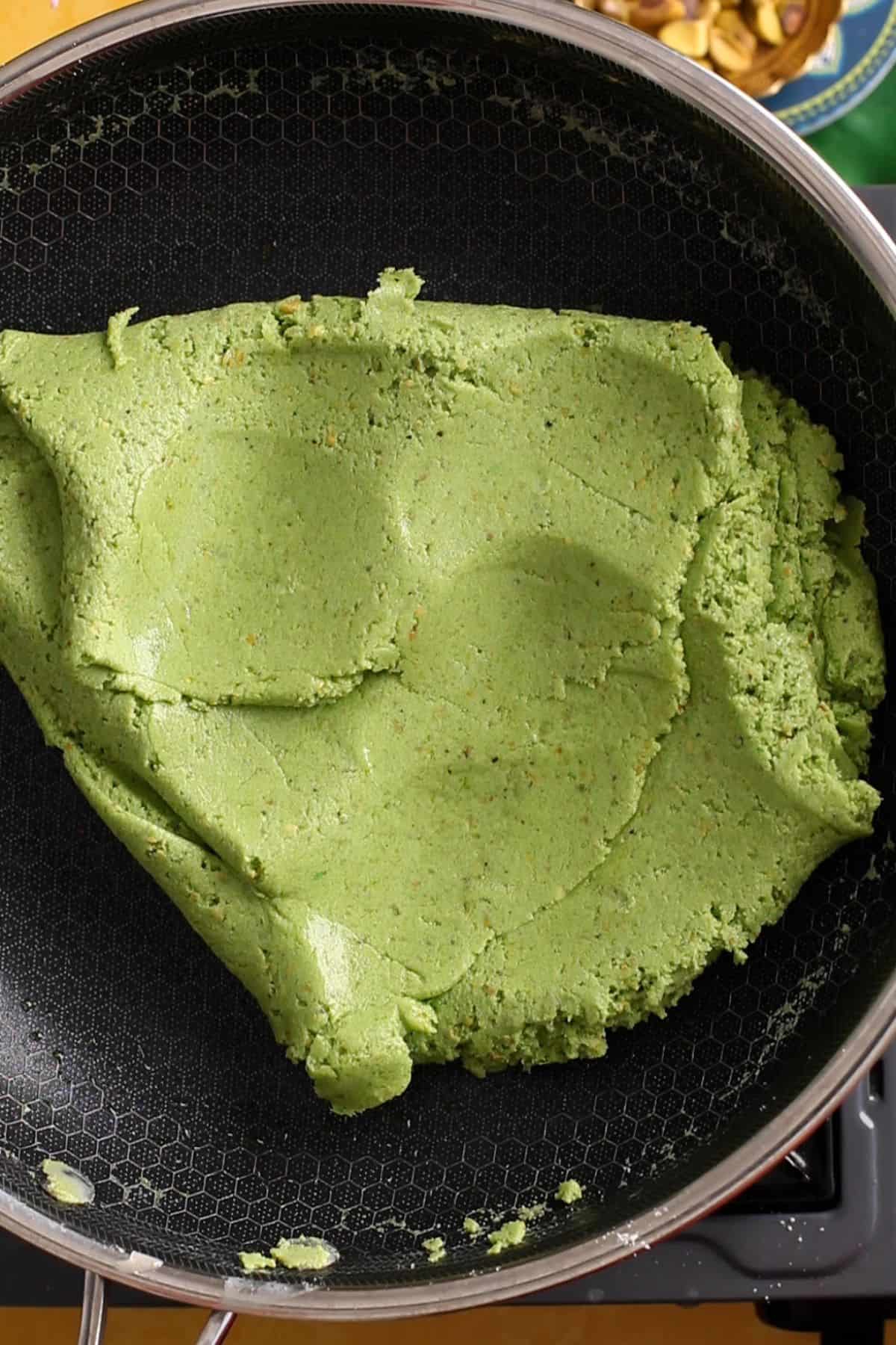 The pistachio burfi mixture is cooked on low heat until it starts leaving sides of pan.