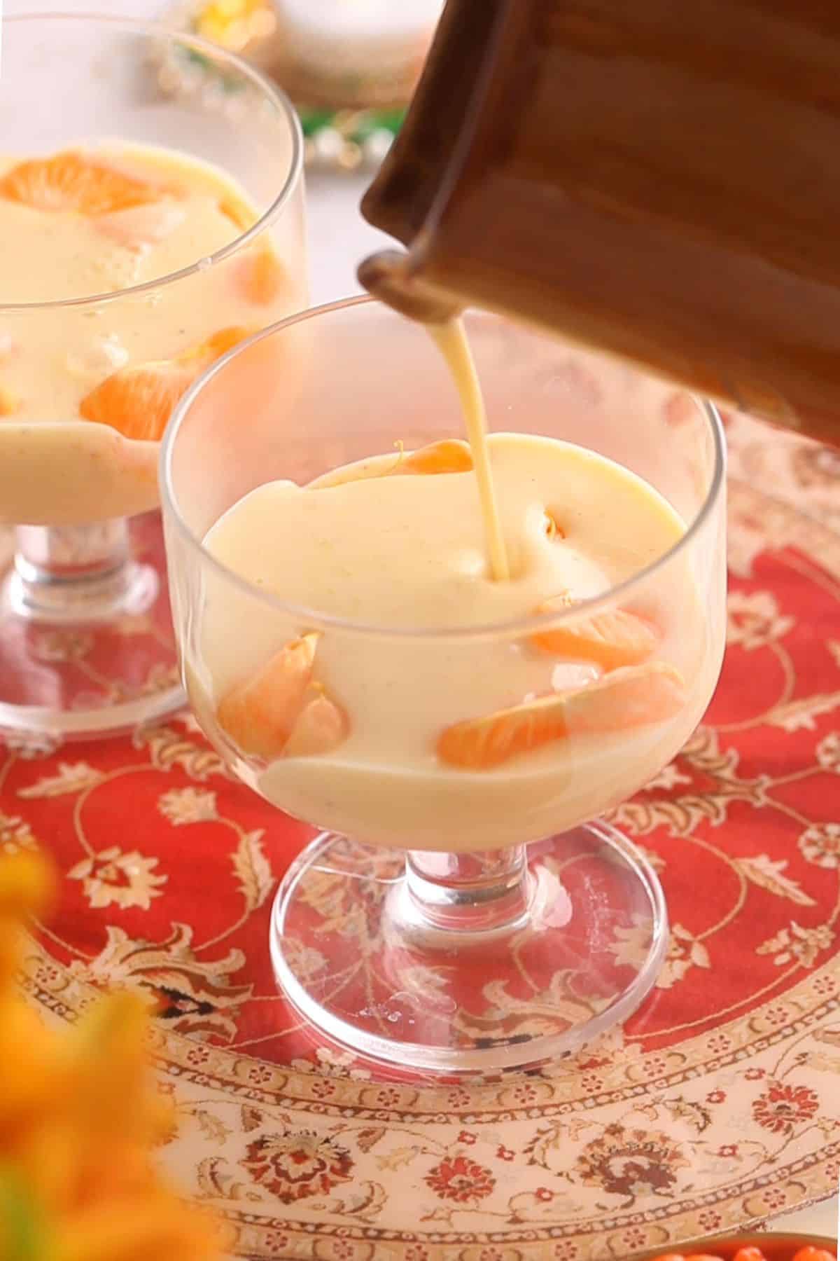 Custard is poured on top of orange slices in a glass dessert bowl.