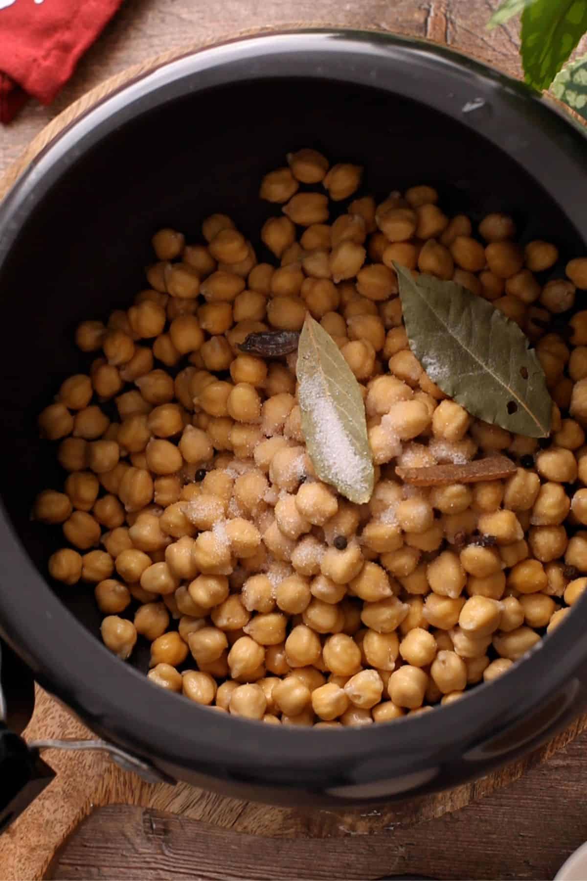 Soaked raw chickpeas with whole spices added to a black pressure cooker. 