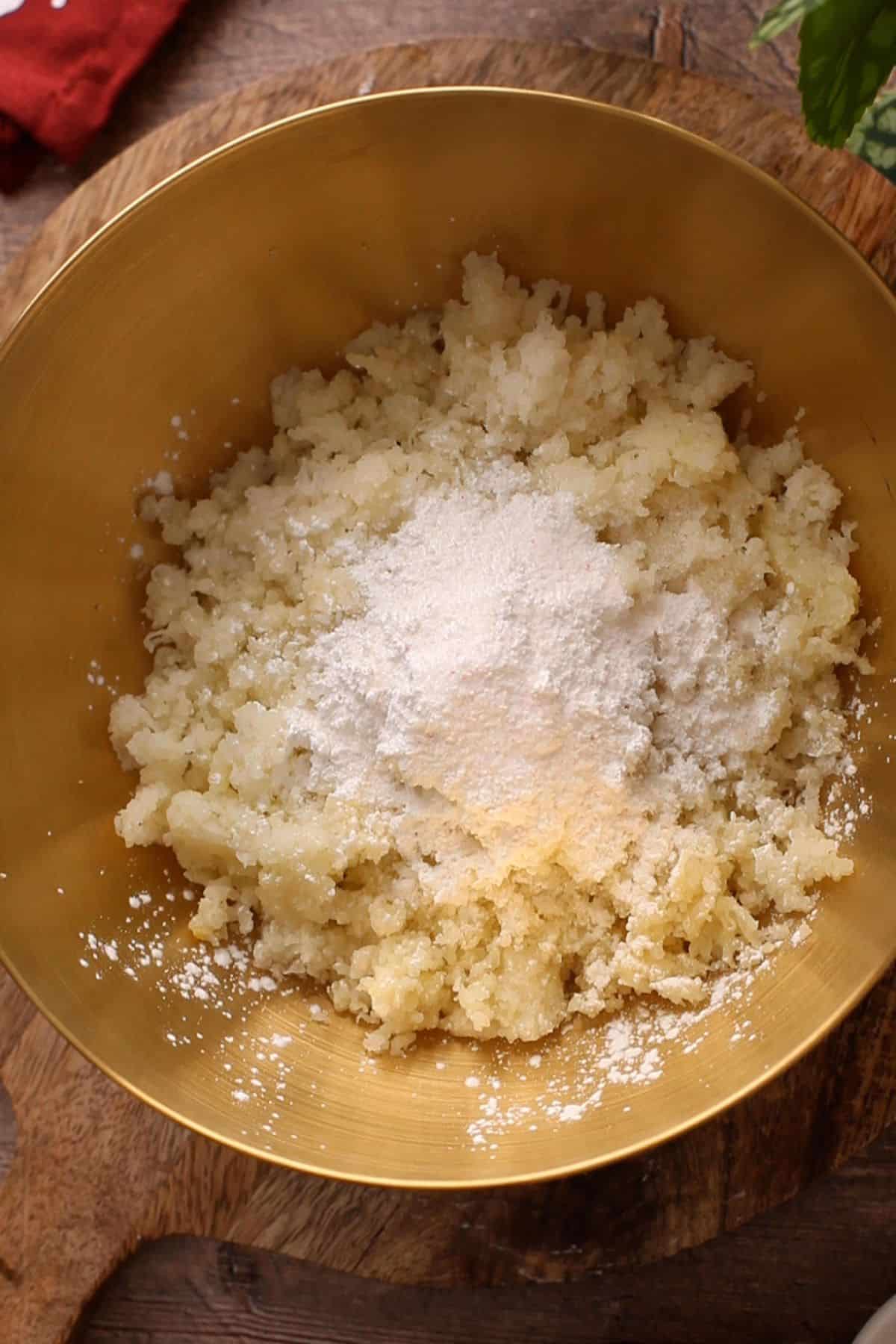 Grated boiled potatoes and cornstarch in a gold mixing bowl.