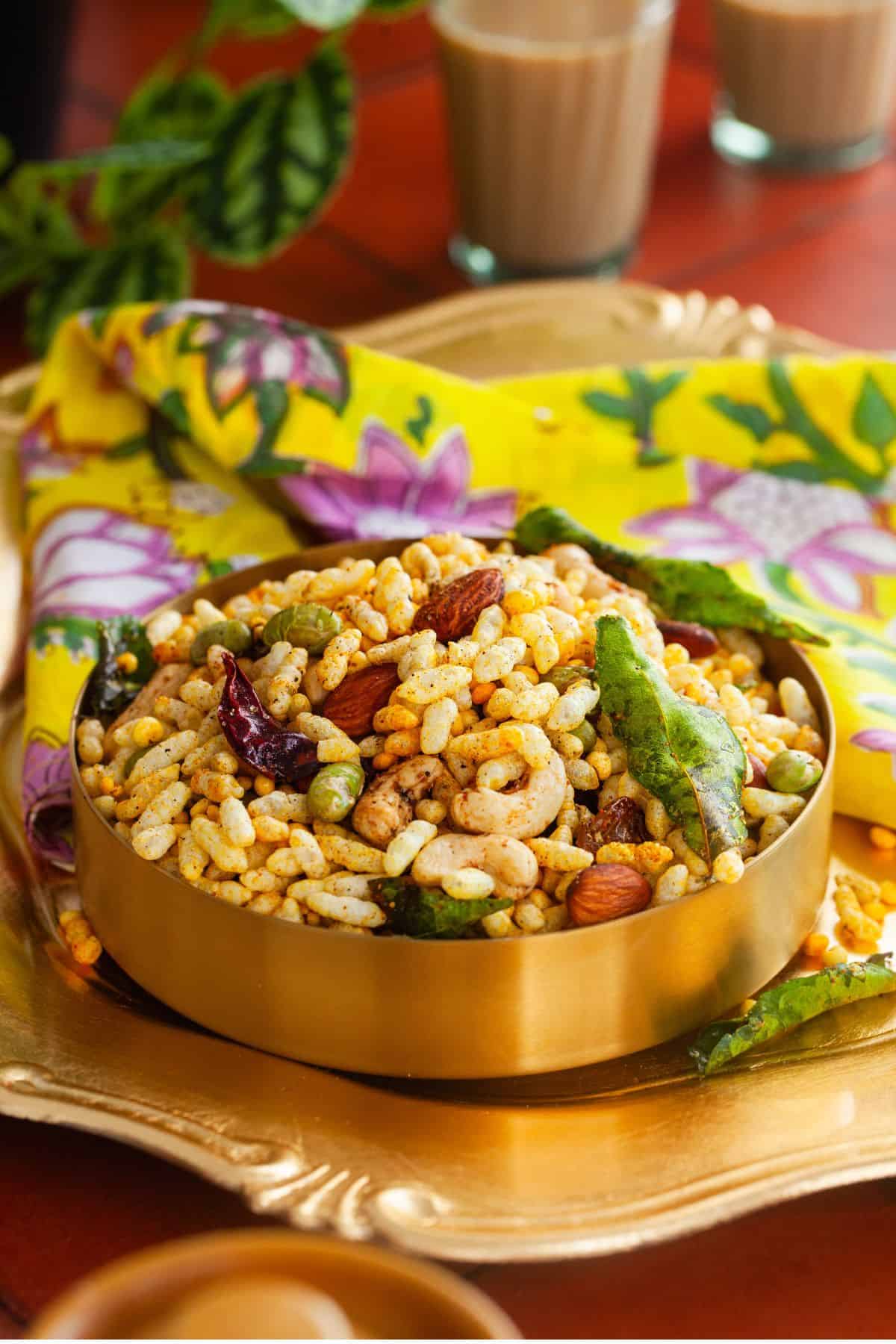Puffed rice chivda served in gold bowl with chai in background. 