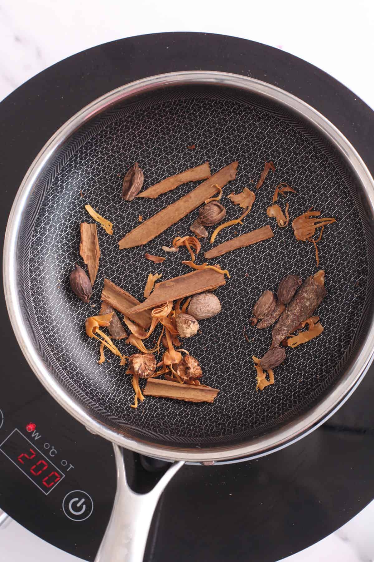 Roasting black cardamom, nutmeg, cinnamom and mace in a black pan.
