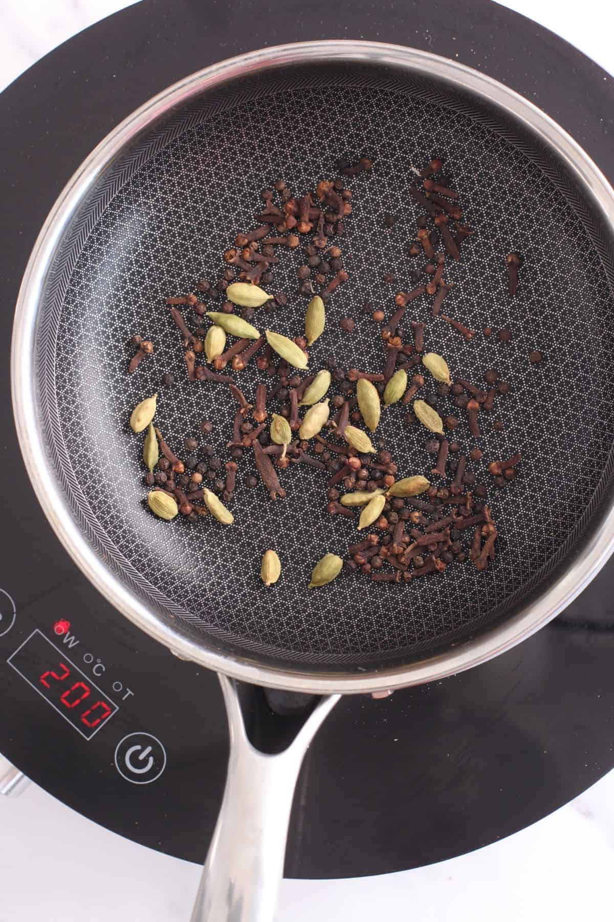 Roasting green cardamom, cloves and peppercorns in a black pan.