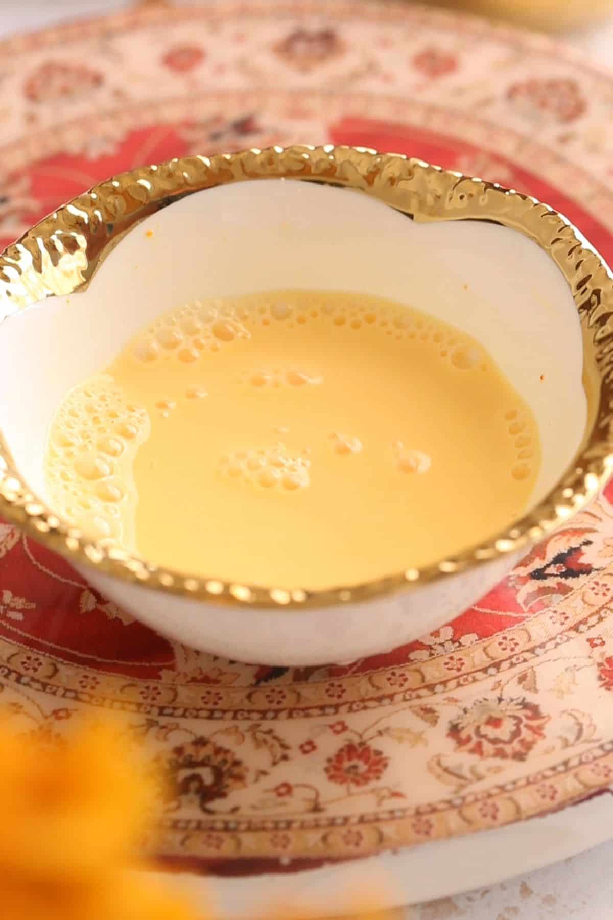Custard powder & milk mixture in a gold rimmed white bowl.