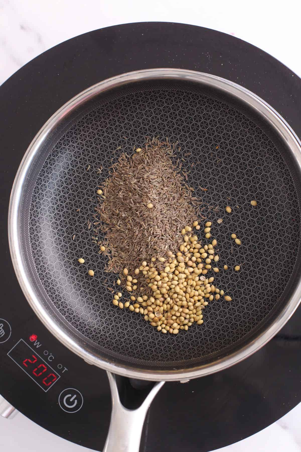 Roasting shahi cumin and coriander seeds in a black pan.