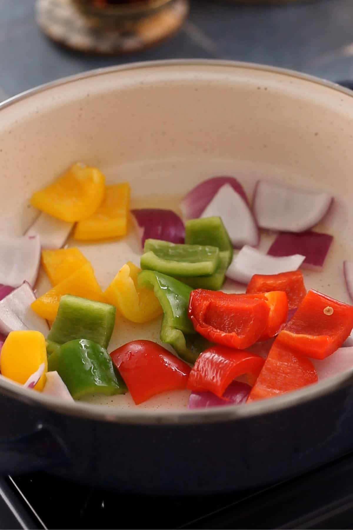 Bell peppers and onion petals are added to a cooking pot.