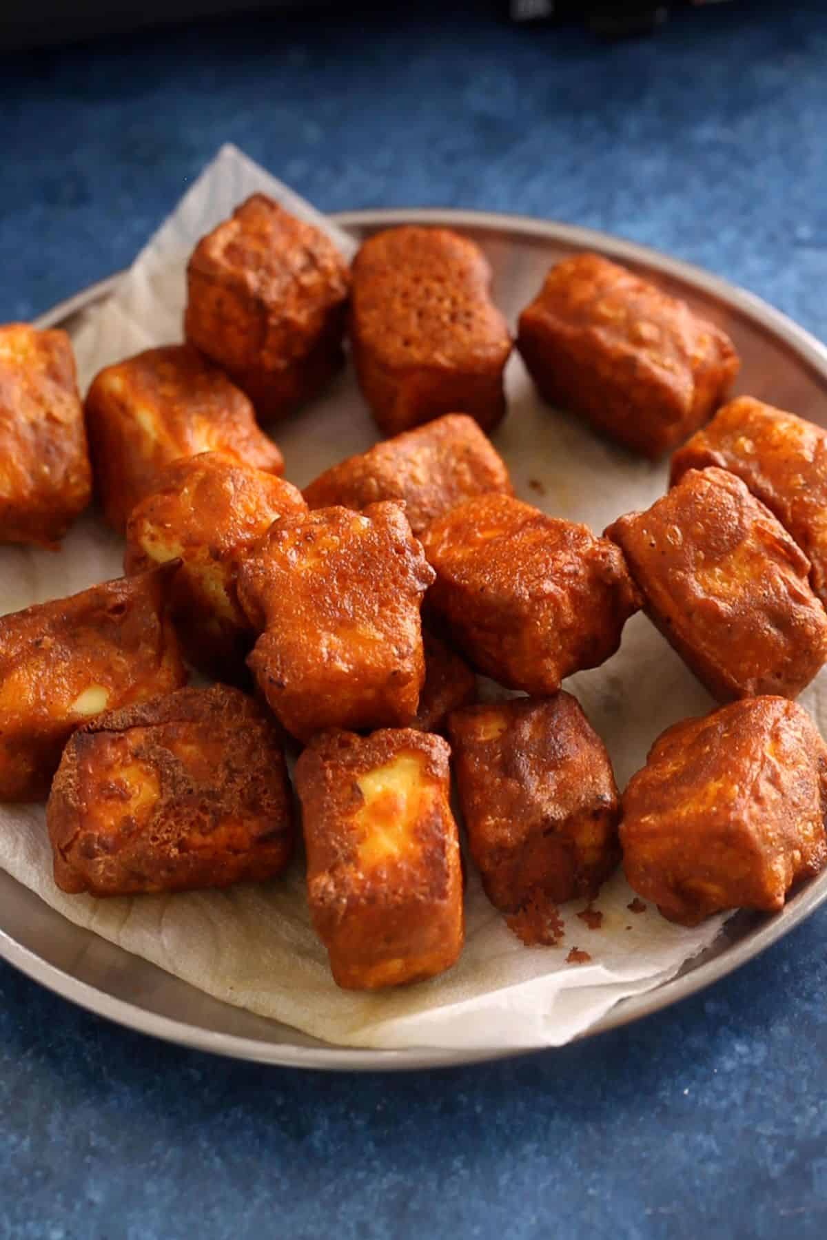 Fried crunchy paneer cubes are drained on a paper towel.