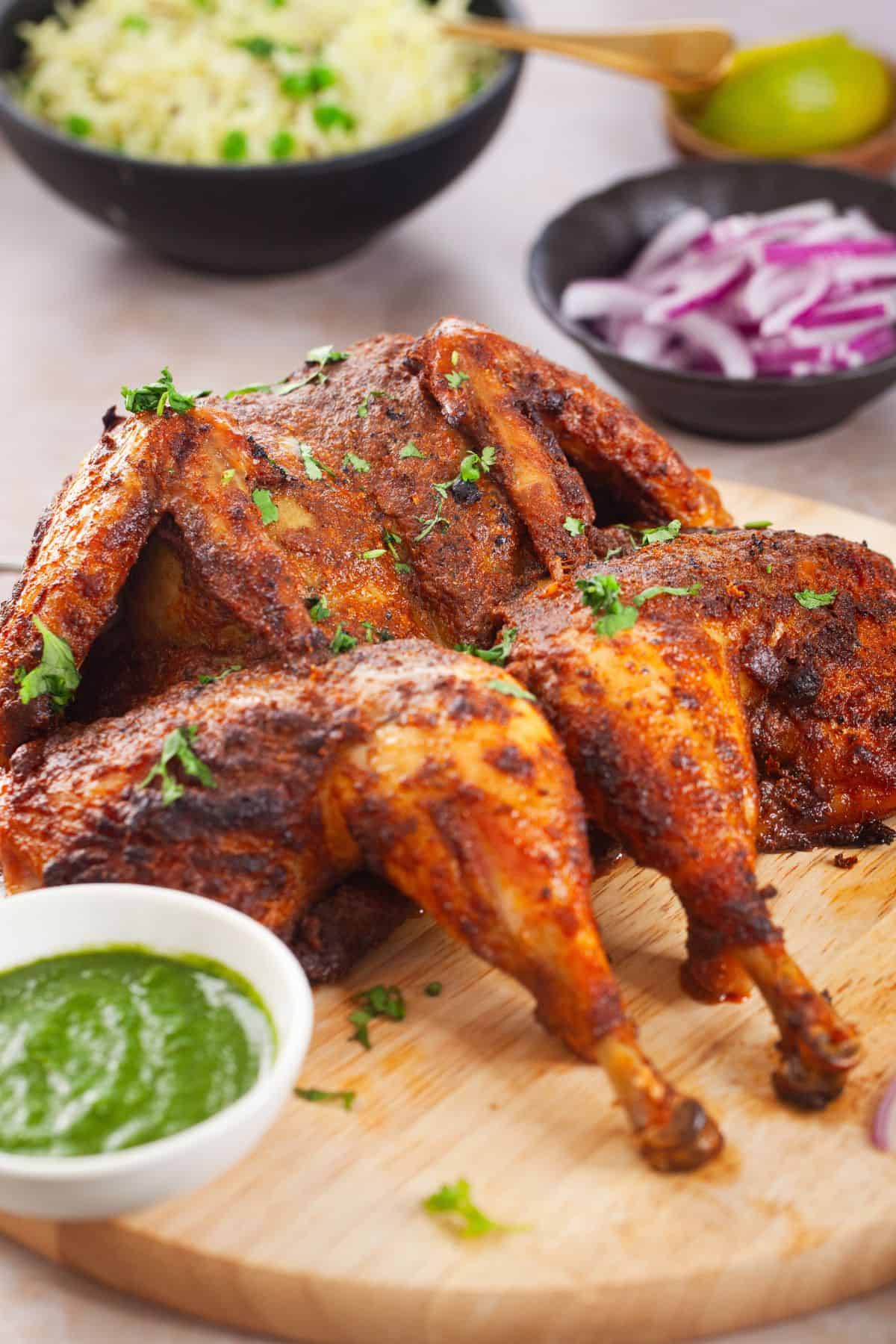 Front view of masala roast chicken with pulao and green chutney in background.