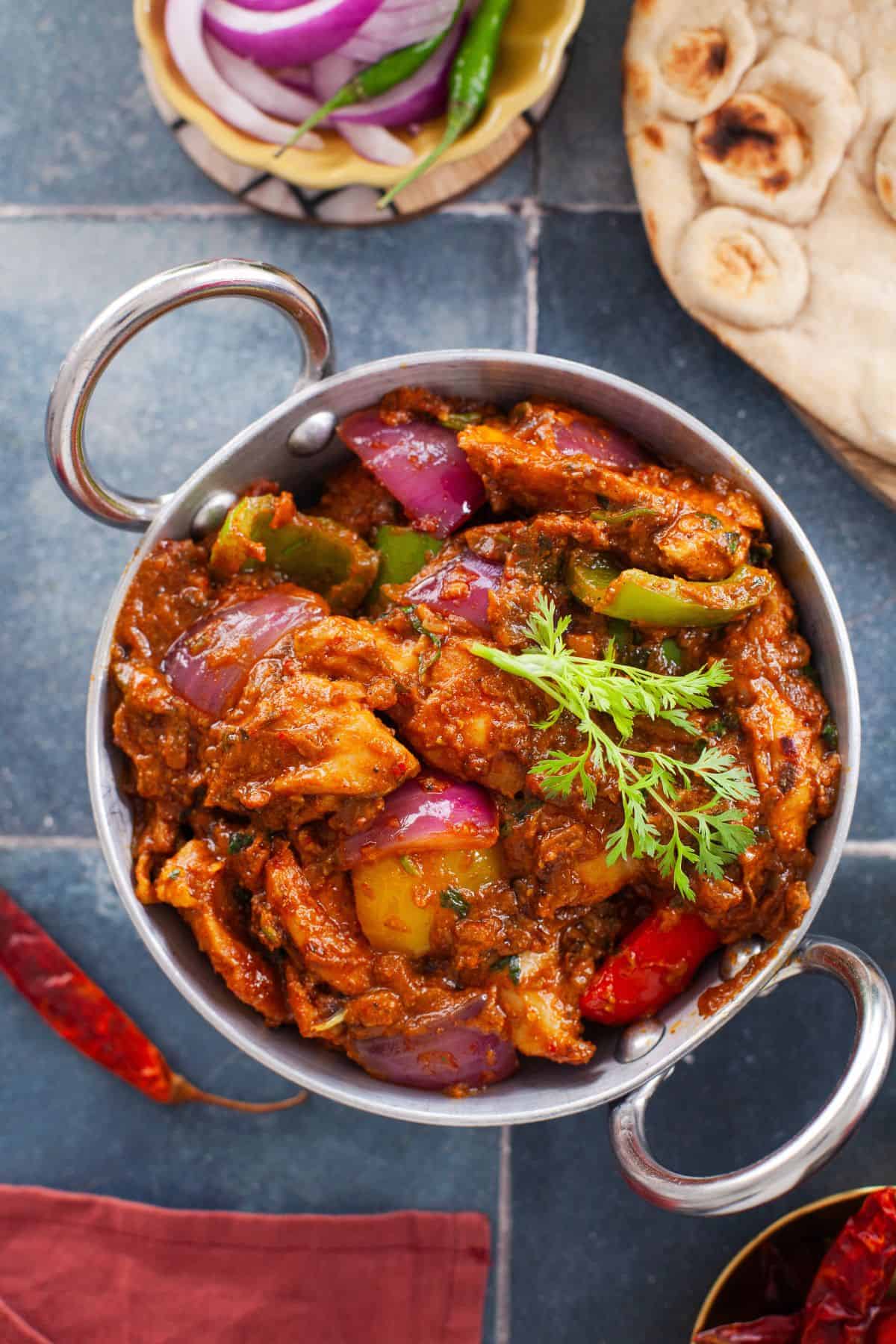 Overhead image of kadhai chicken on a tiled backdrop placed with tandoori rotis.