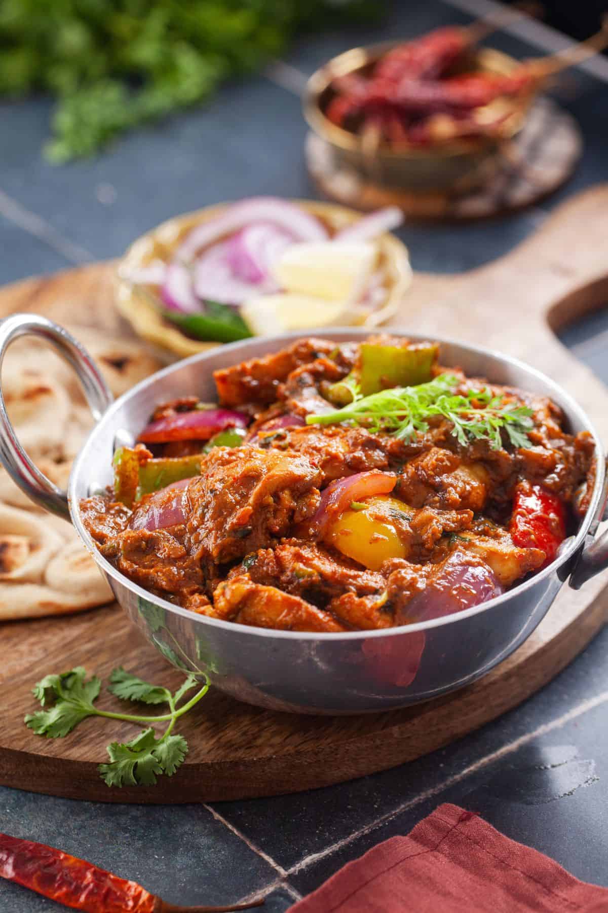 Kadai chicken served in a small kadai with onions and flatbread in the background.