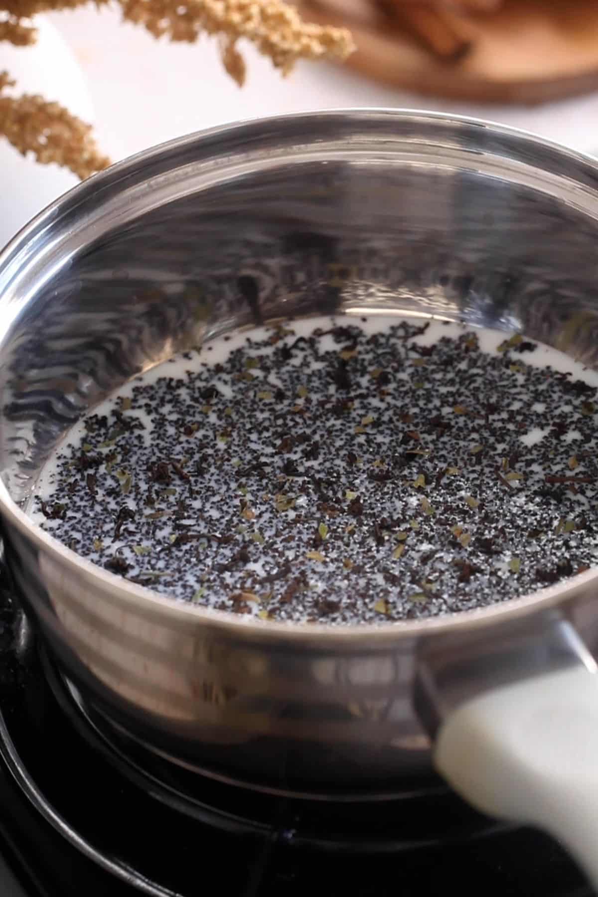 Loose black tea leaves are added to whole milk in a steel pot.