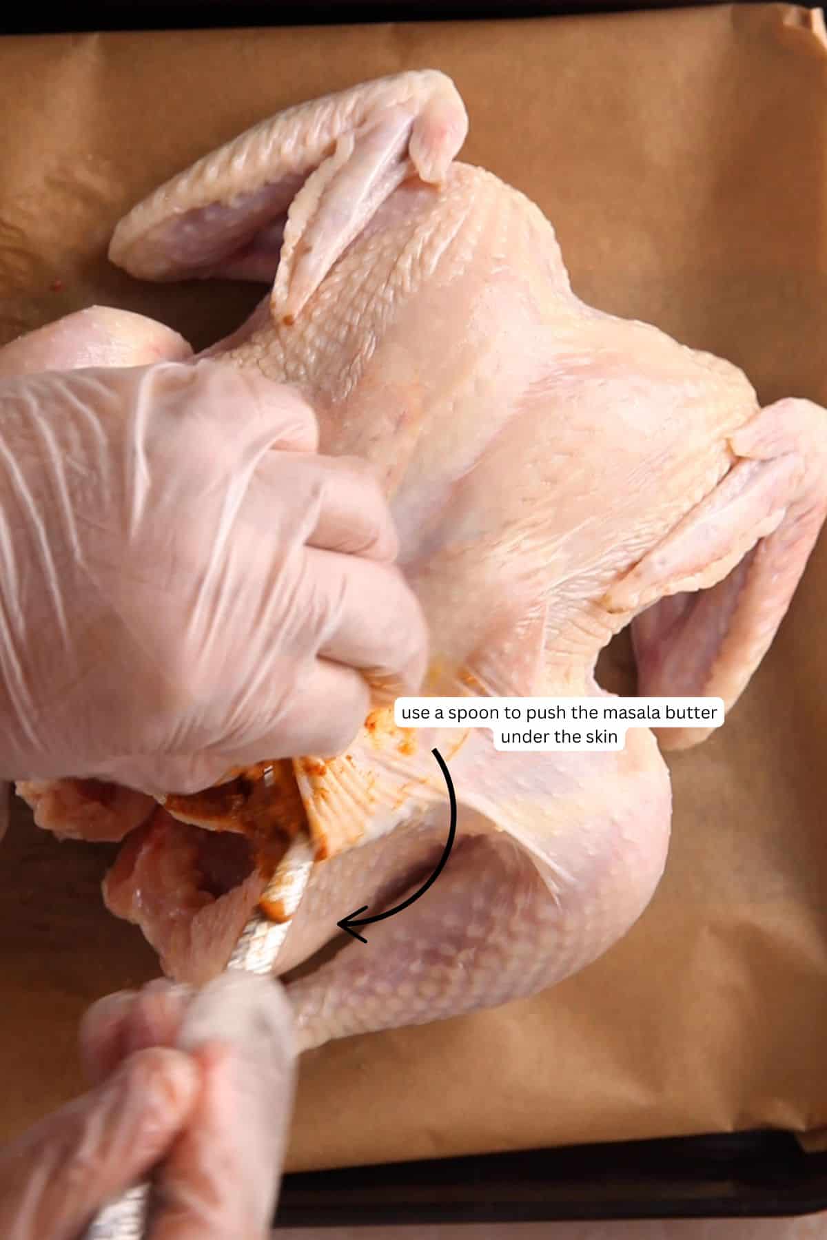 Using spoon to to stuff masala butter under the chicken skin.