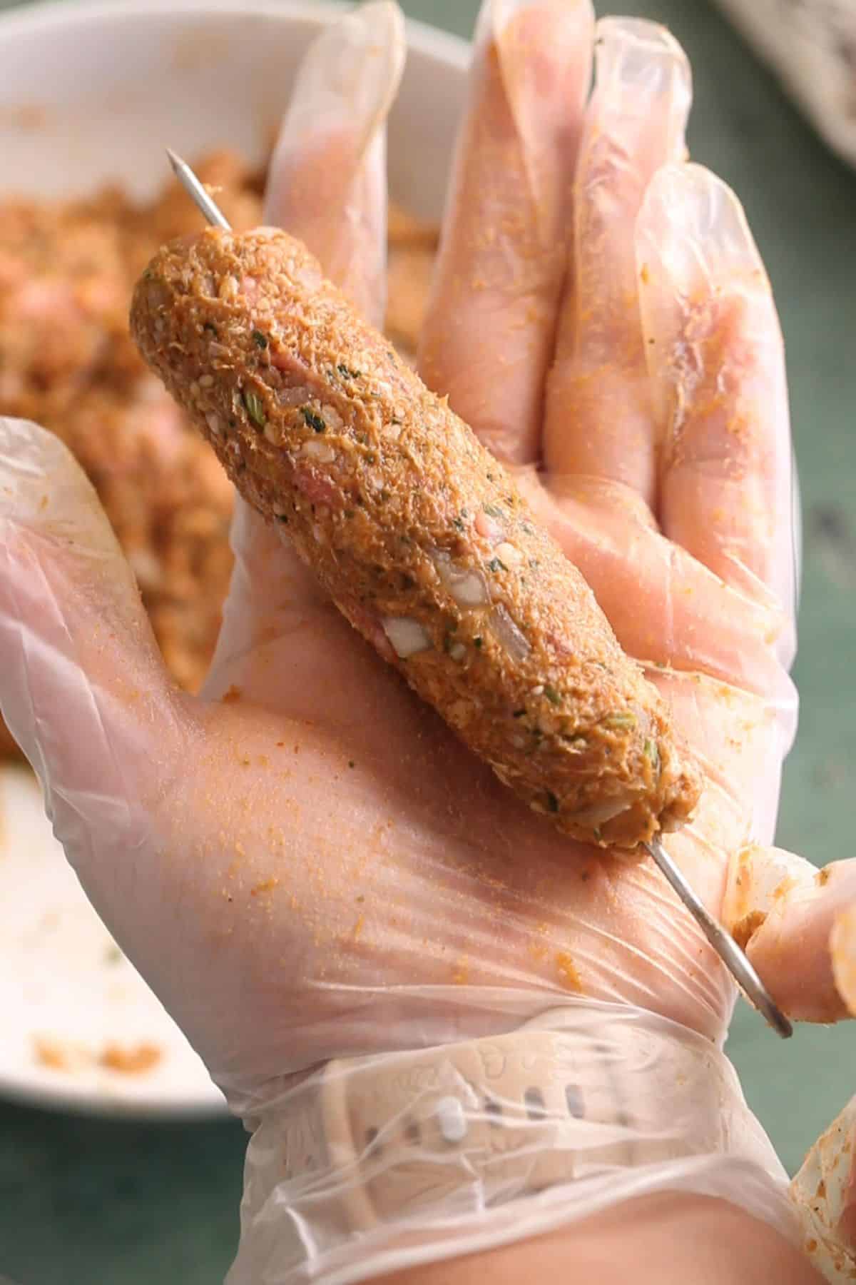 Minced meat mixture is shaped around the skewer to resemble a tube.