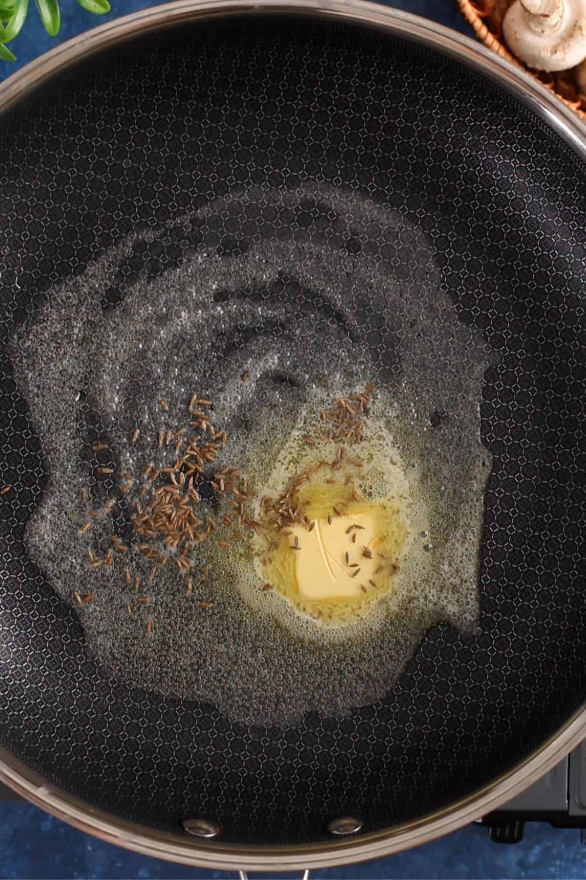 Butter and oil in a black pan with crackling cumin seeds.