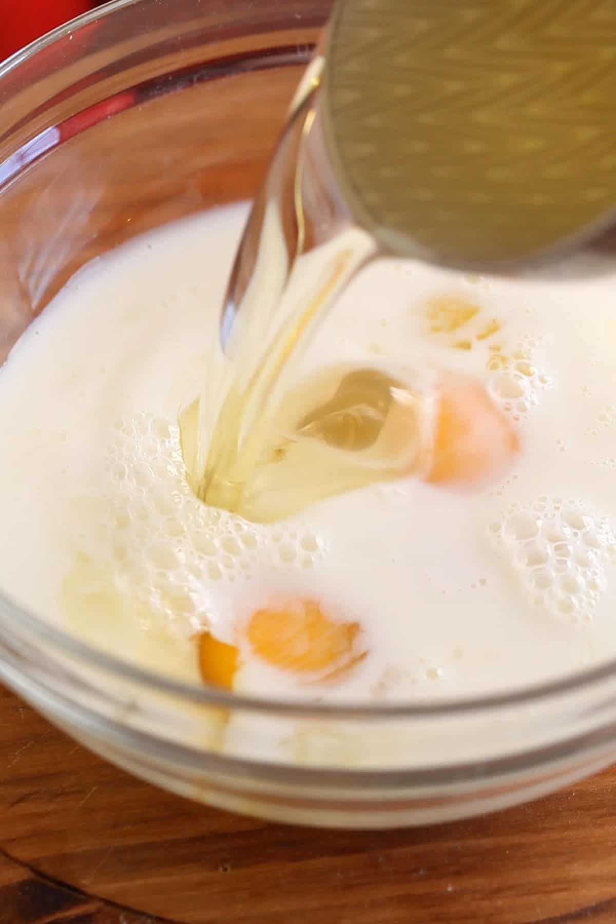Milk, whole eggs and oil are added to a glass bowl.