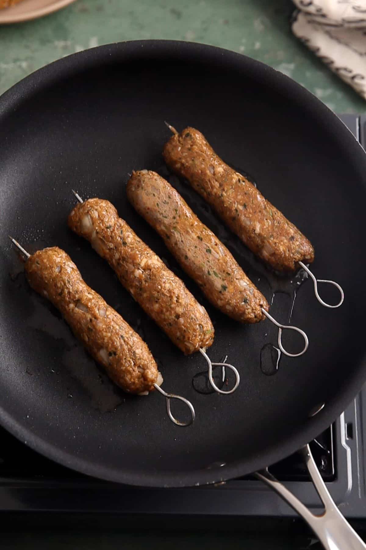 Seekh kebabs are placed in a black pan for cooking.