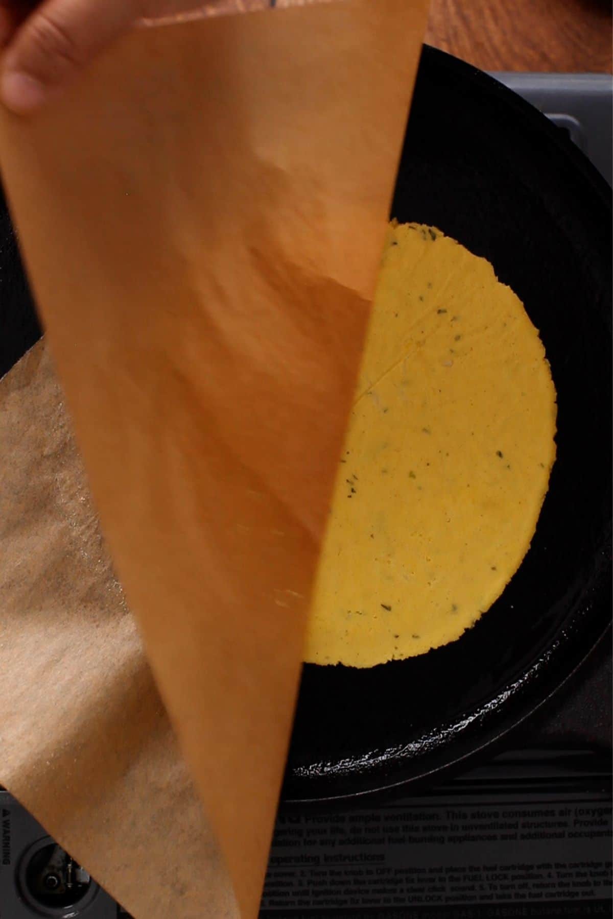 Corn meal flatbread is placed on griddle and parchment paper is peeled away. 