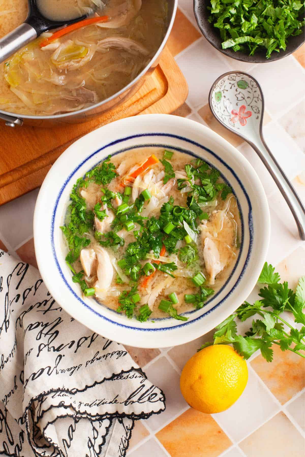 Chicken Soup With Cilantro and lemom served in a white bowl with blue rim.